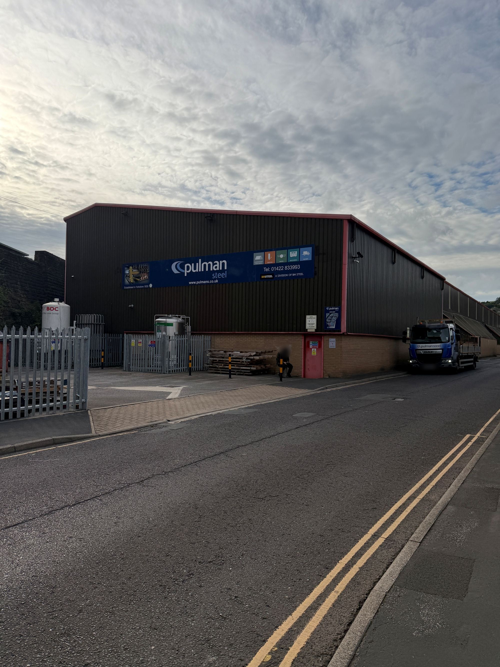 A large dark-clad steel warehouse with a blue Pulman Steel sign reading &ldquo;Established in Yorkshire 1830&rdquo;.