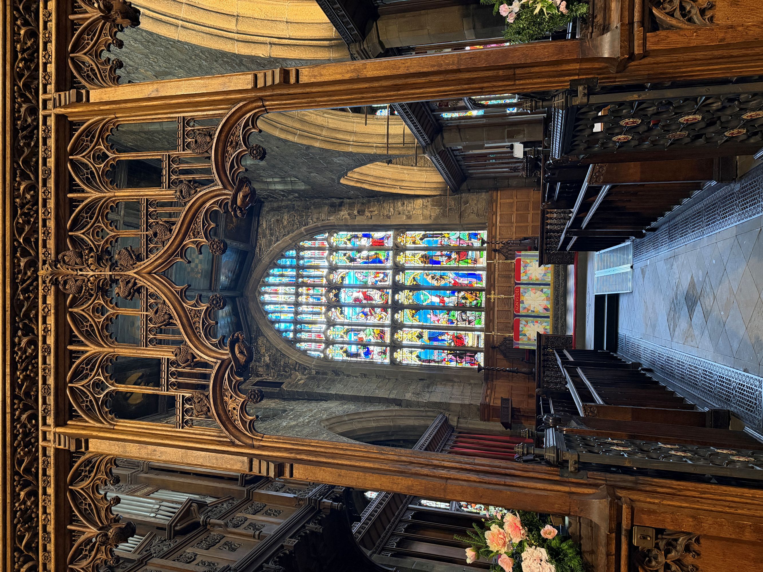 Looking east through a carved oak screen to the chancel, with a large stained-glass east window above the altar.